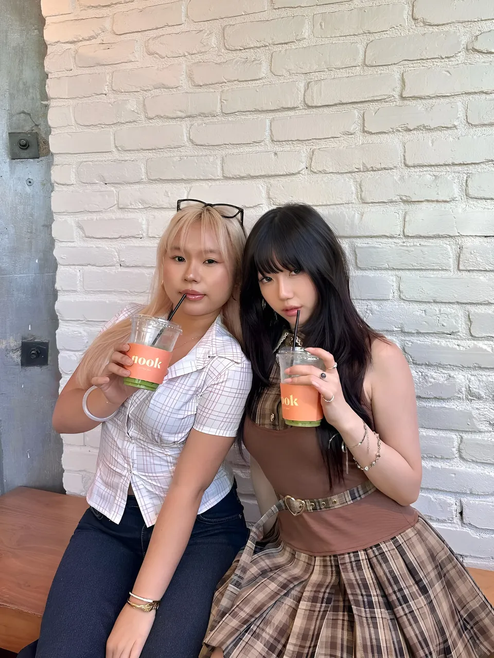 Mina Hartley — Two people holding drinks while seated against white brick wall