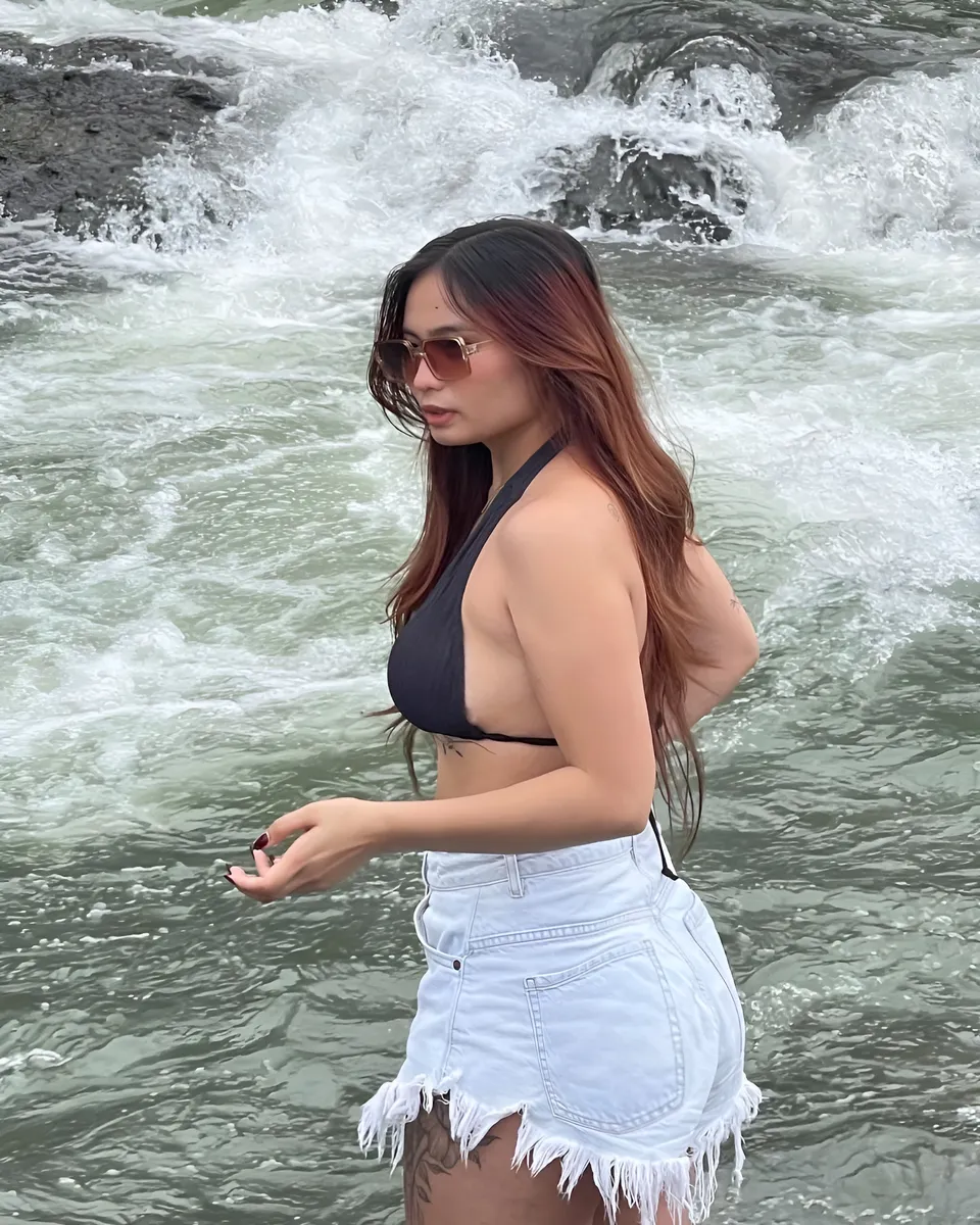 Mira Collins wearing black top and white shorts in flowing water