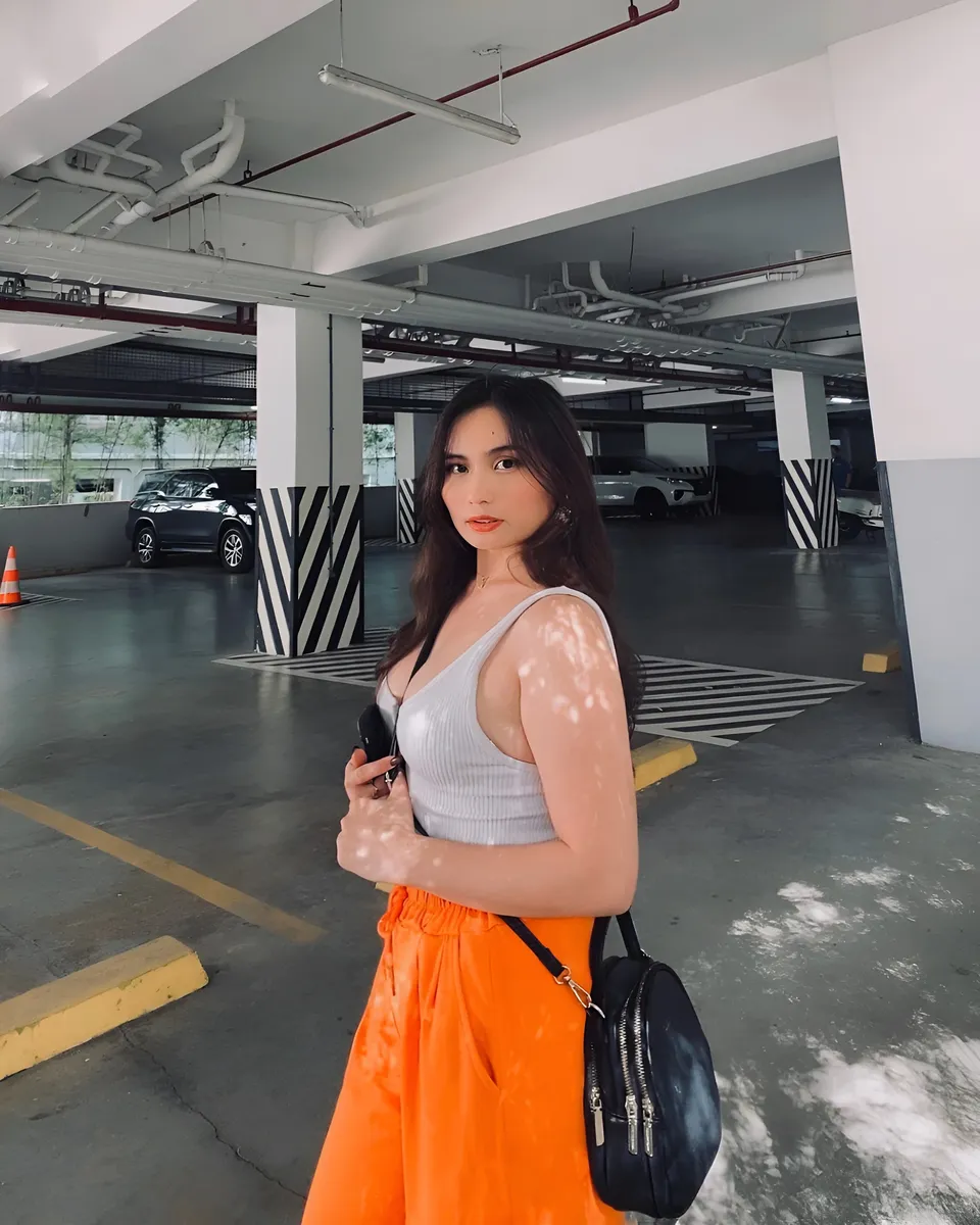 Mira Collins in white top and orange pants stands in parking garage