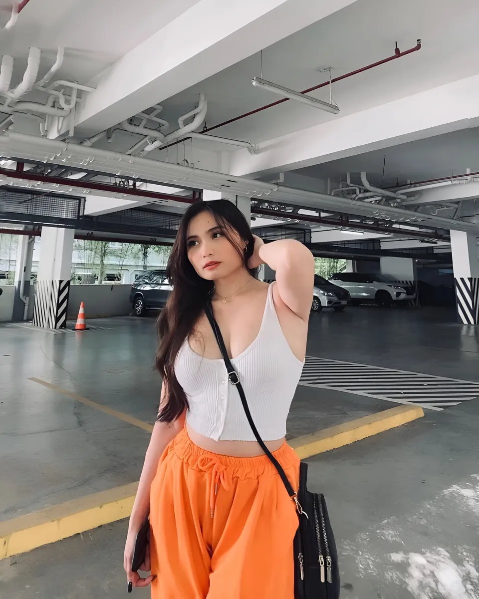 Mira Collins in white top and orange pants stands in parking garage