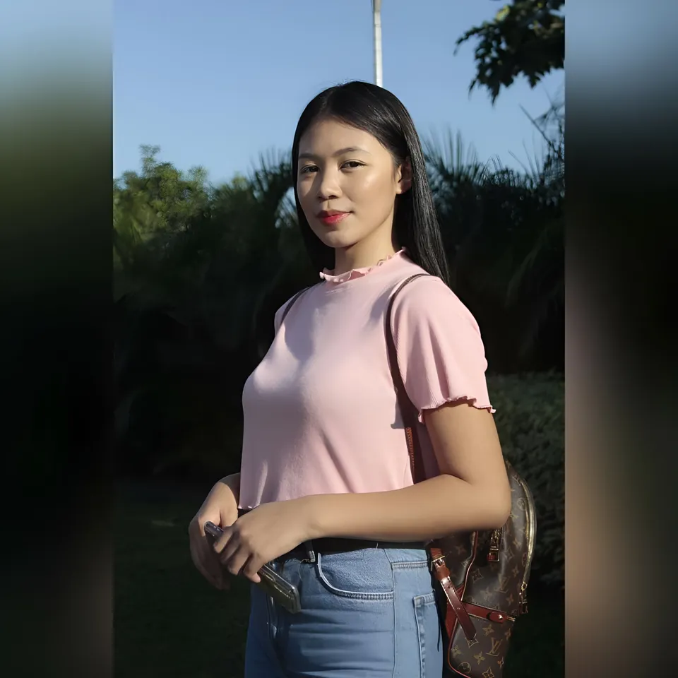Moraya Ong in pink top and jeans stands outdoors with bag