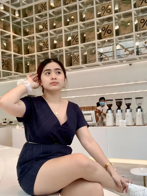 Pamela Tanbua in dark pinstripe dress sits in coffee shop