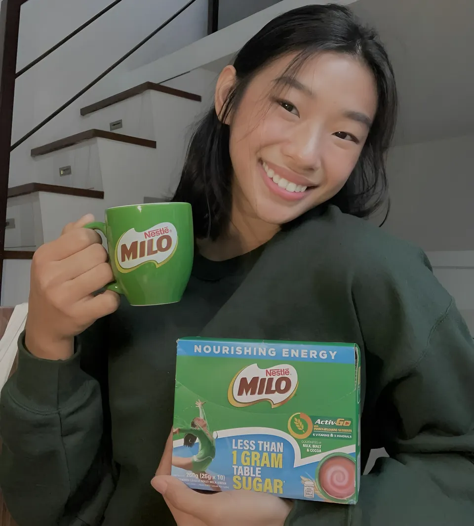 Pia Idelfonso holding green mug and Milo box in front of staircase
