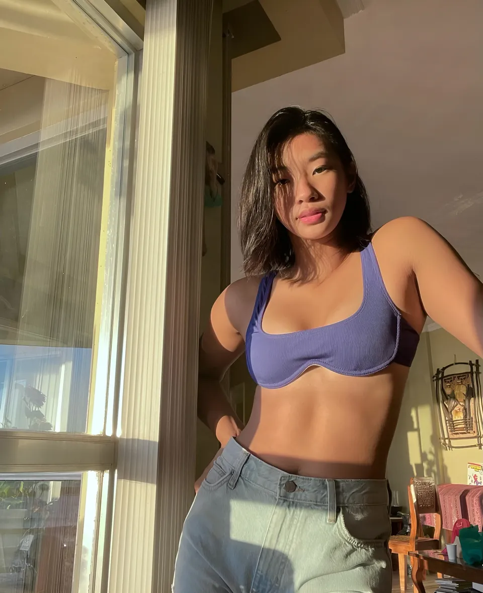 Pia Idelfonso in purple top and jeans standing near window