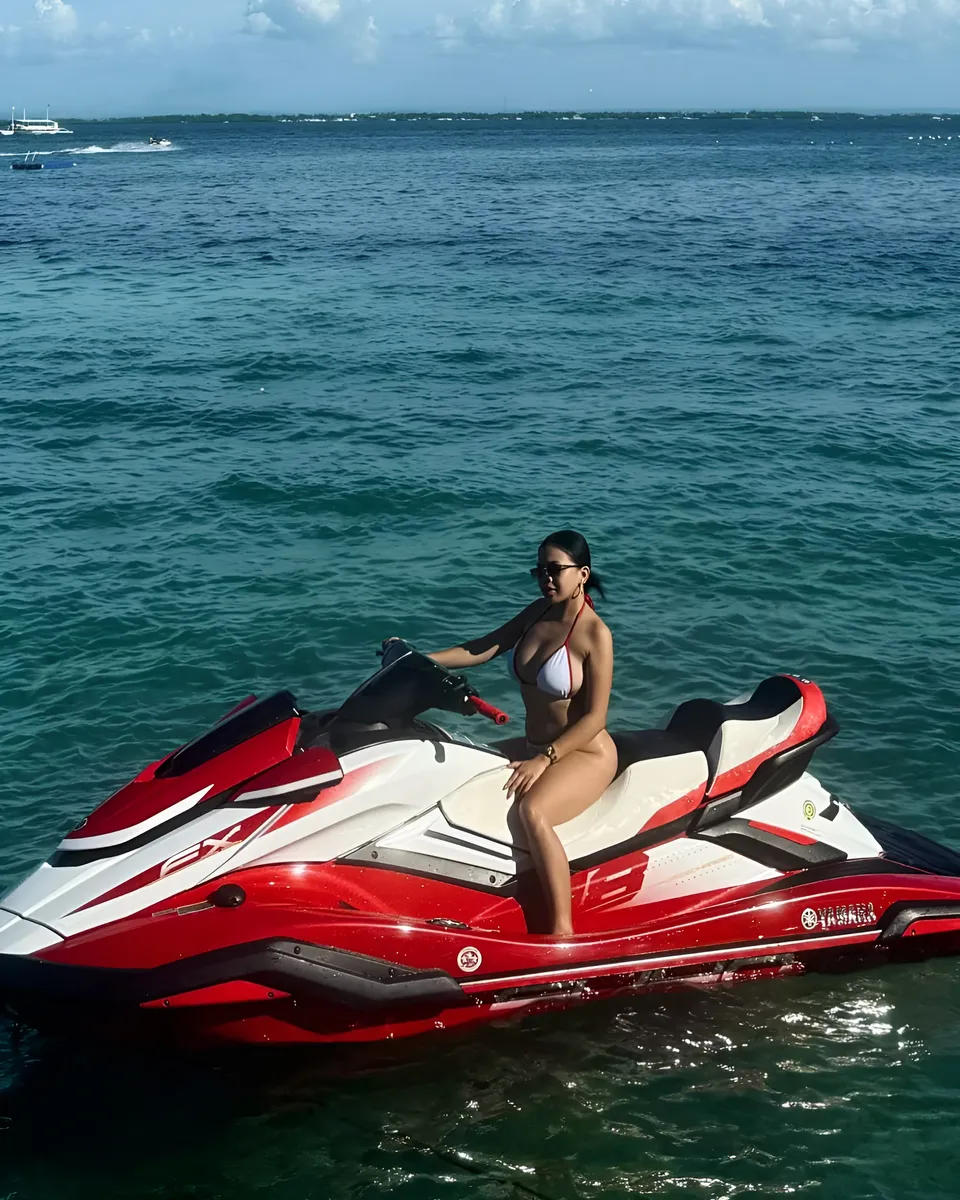 Piper Quinn in bikini seated on red and white jet ski on water