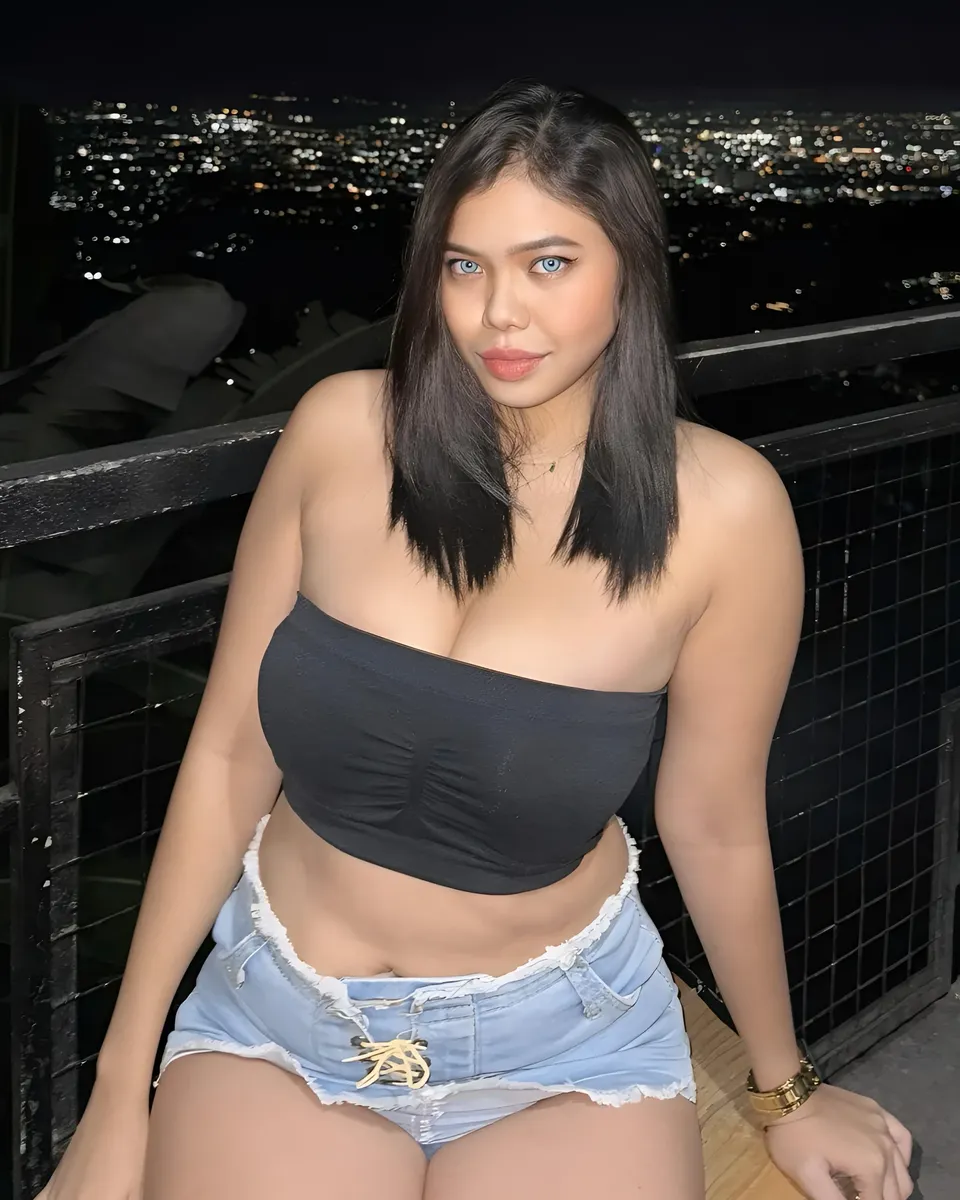 Piper Quinn in black top and denim shorts seated on balcony at night