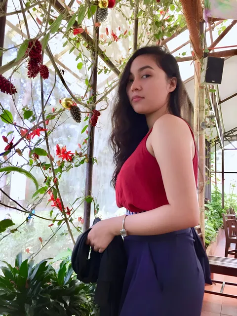 Princess Mae in red top and blue pants stands under flowering vines