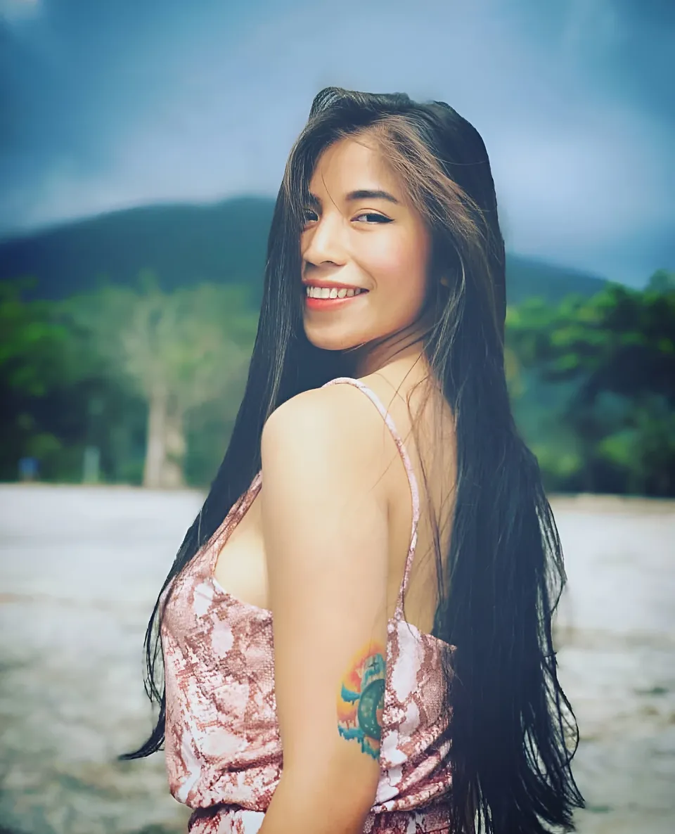 Princess Reyes in pink patterned top smiles over shoulder at beach