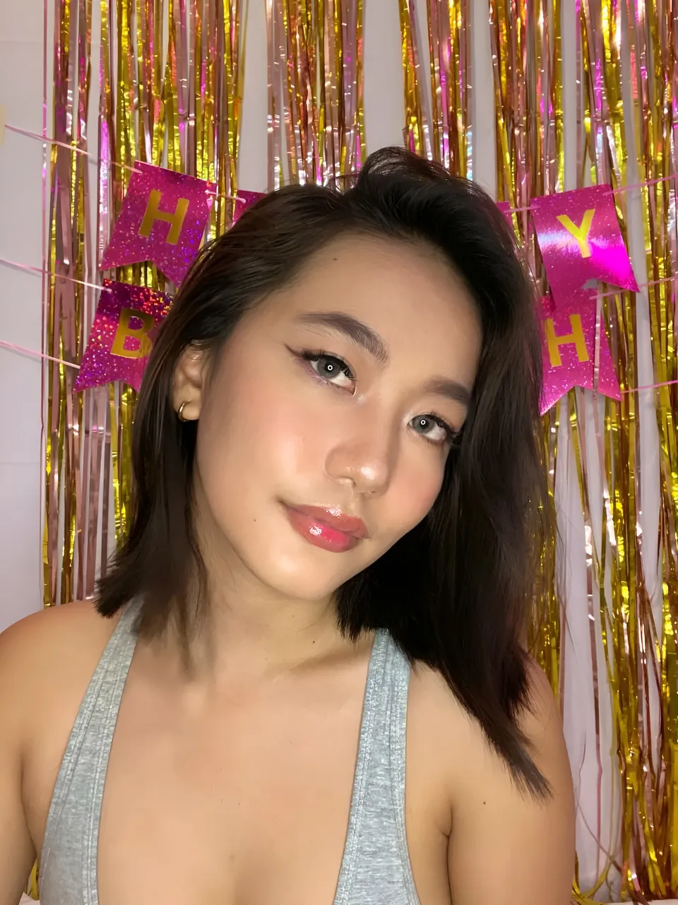 Ramoana Sinclair in gray top poses in front of gold and pink streamers