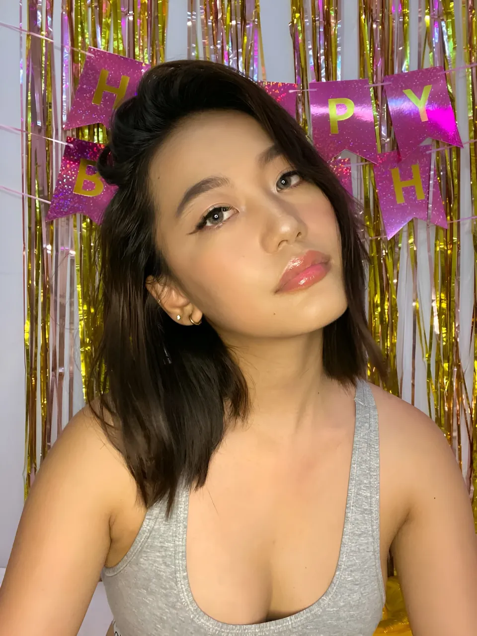 Ramoana Sinclair in gray top poses in front of gold and pink birthday decorations