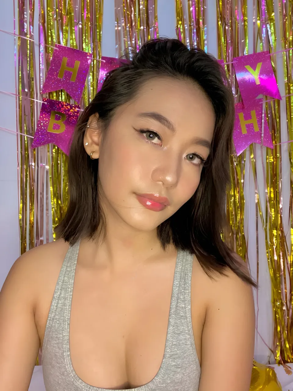 Ramoana Sinclair in gray top poses in front of pink and gold birthday banner