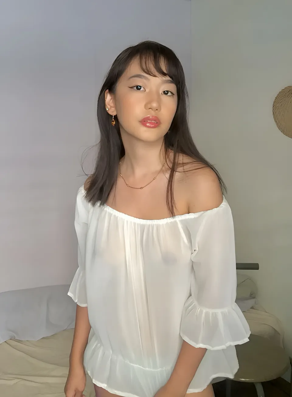 Ramoana Sinclair wearing white off-shoulder top seated on bed