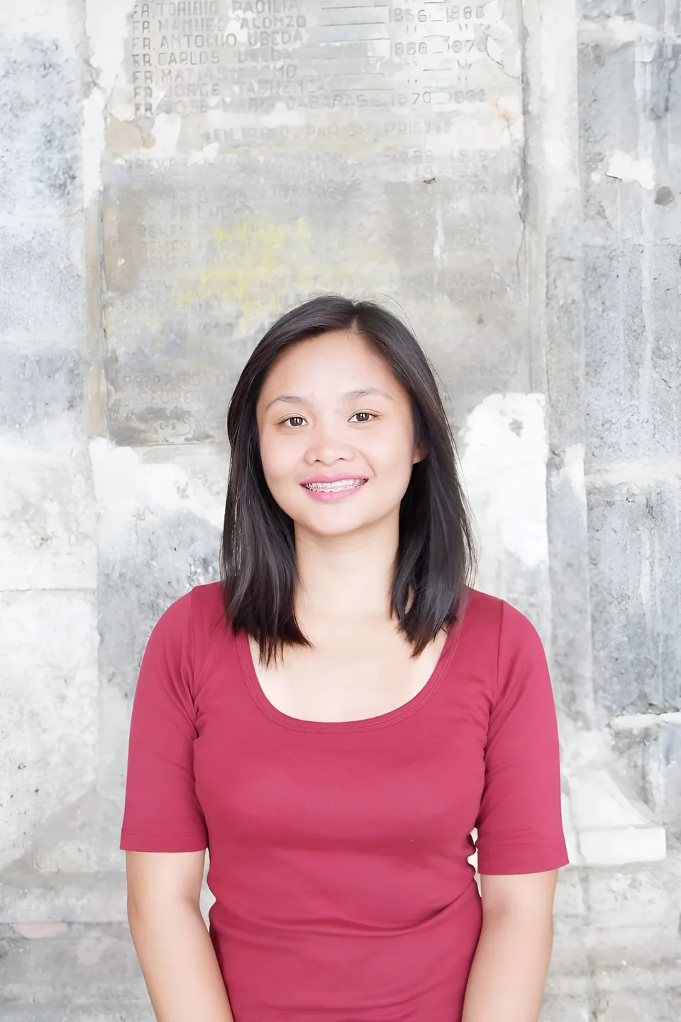 Roxanne Ellery in red top standing in front of stone wall with engraved text
