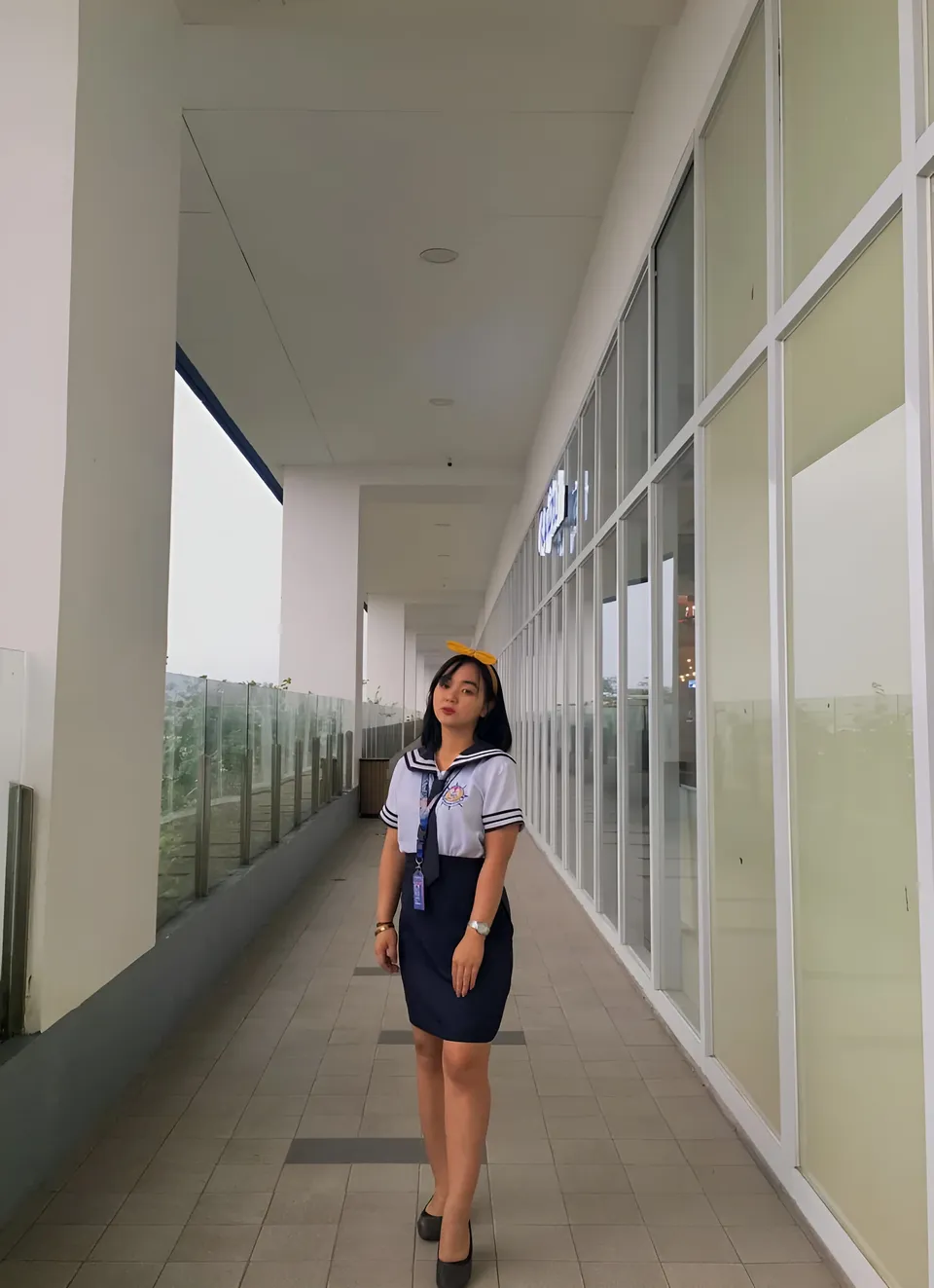 Sakura Keyema in navy skirt and sailor top stands in covered hallway
