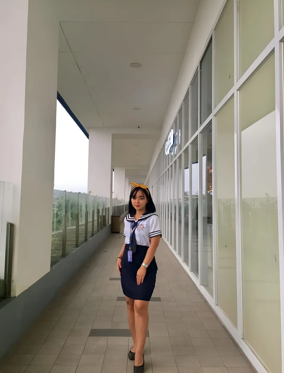 Sakura Keyema in navy skirt and sailor top stands in long hallway
