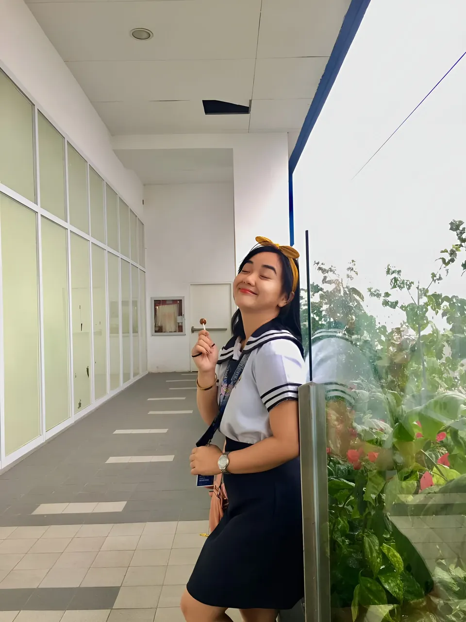 Sakura Keyema in sailor top and skirt standing in hallway near plants
