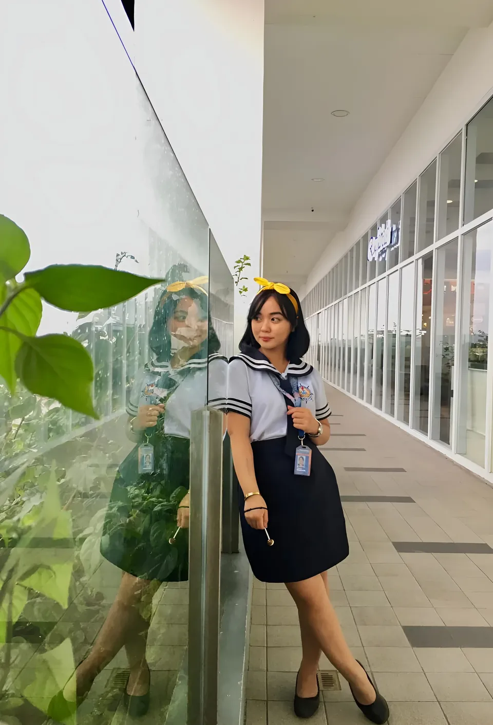 Sakura Keyema in sailor uniform standing beside glass wall
