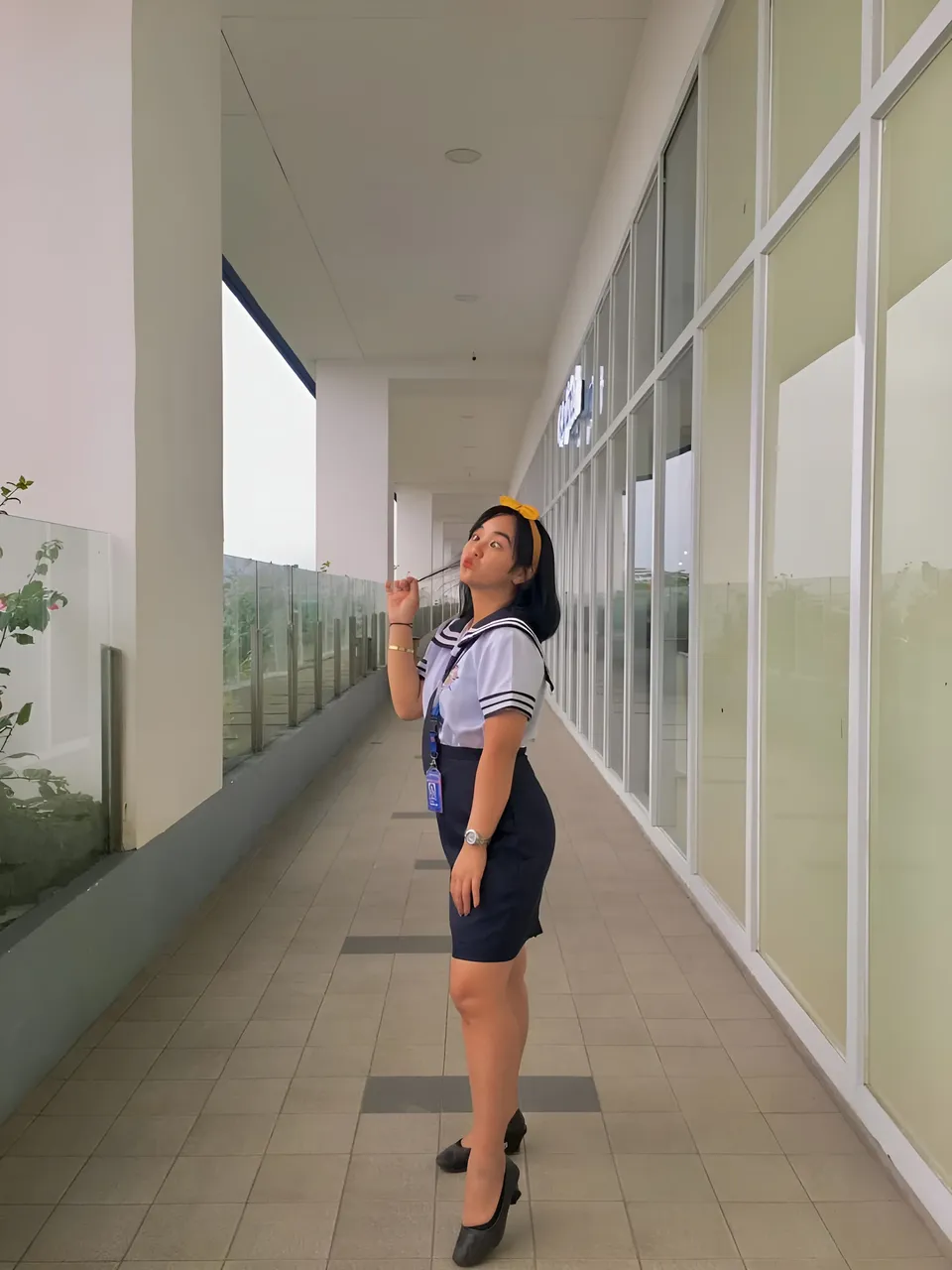 Sakura Keyema in navy skirt uniform standing in long indoor hallway