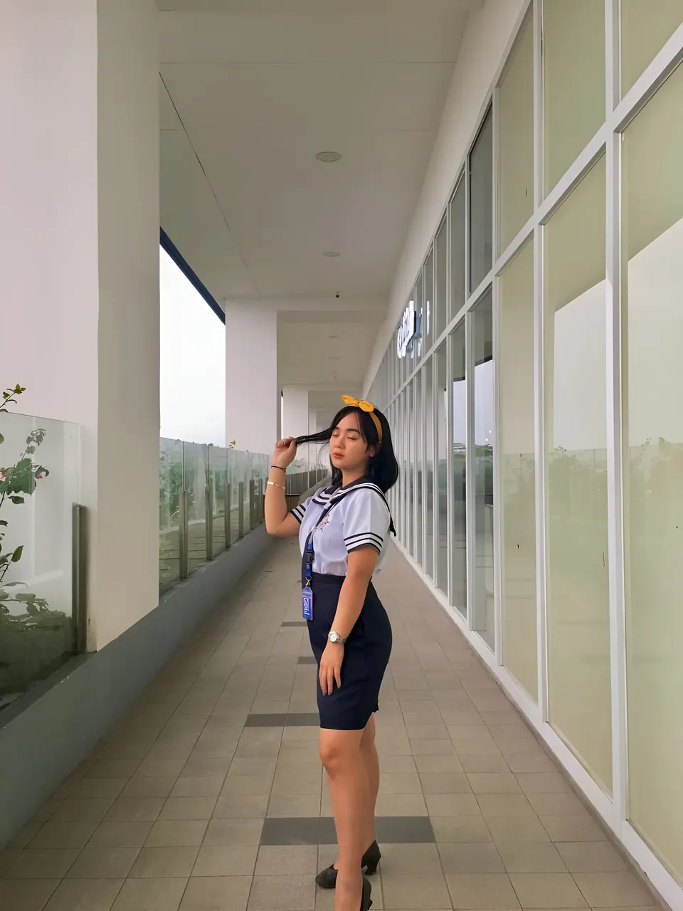 Sakura Keyema in navy skirt uniform standing in long indoor hallway