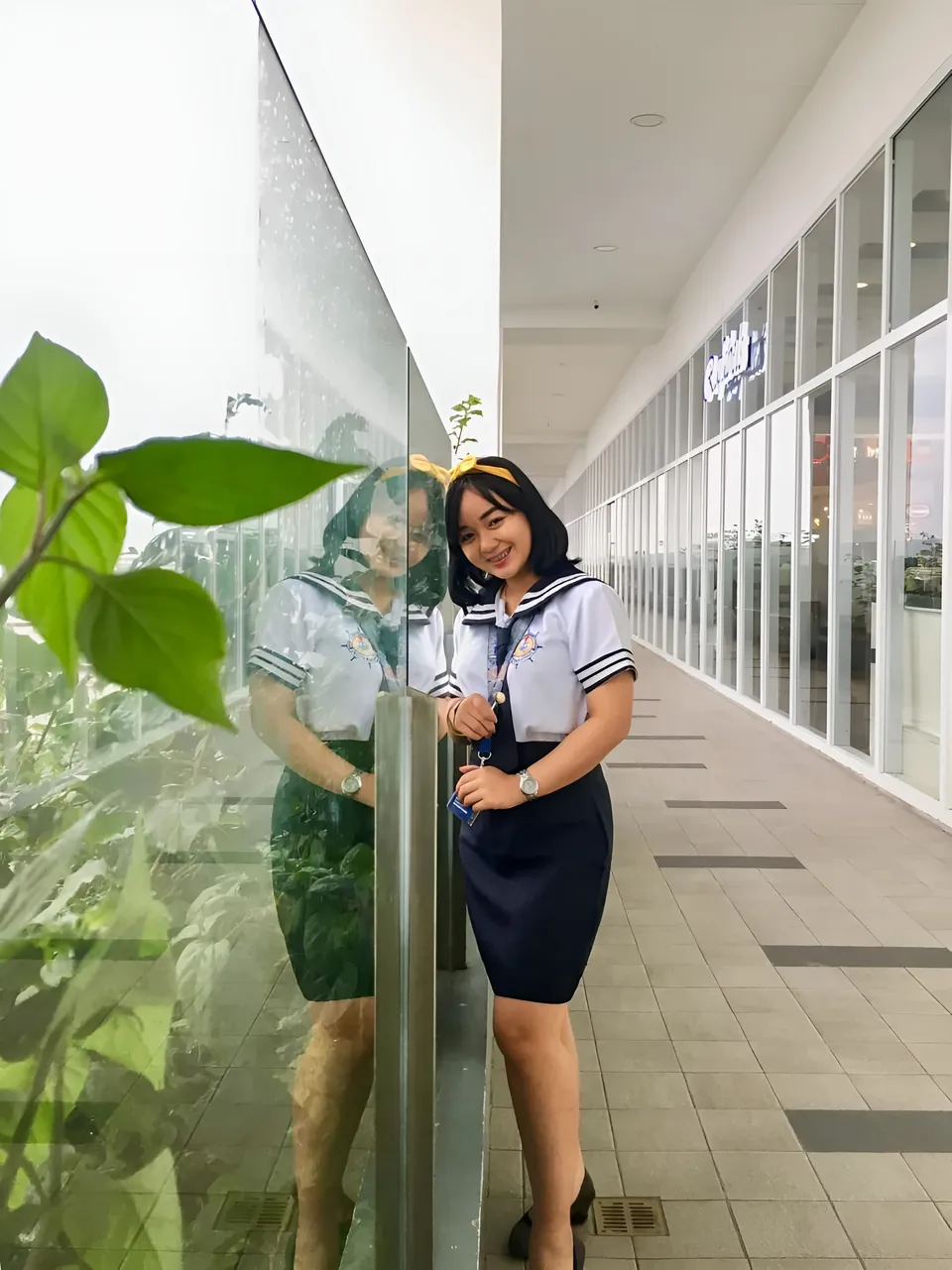 Sakura Keyema in sailor uniform standing beside glass wall