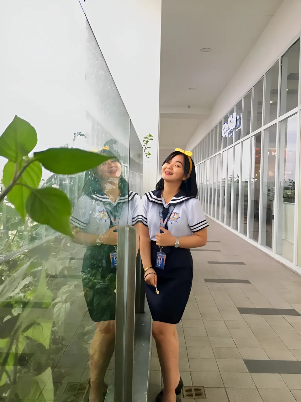 Sakura Keyema in sailor-style top and skirt standing beside glass wall