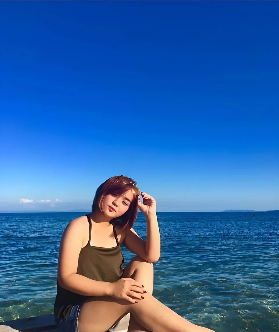 Sakura Keyema sitting by ocean wearing olive top and shorts