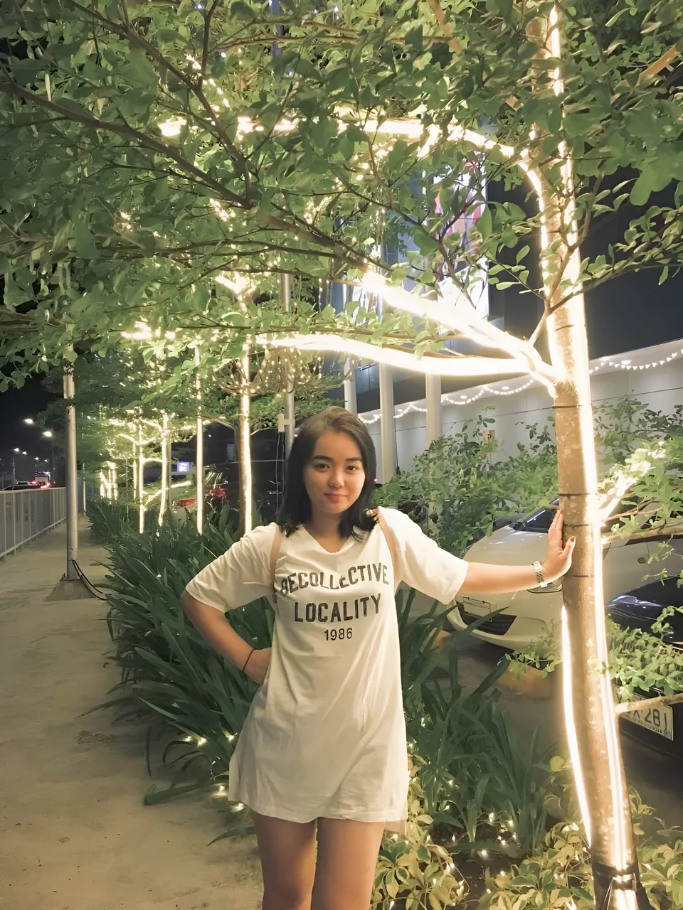 Sakura Keyema in white t-shirt standing under illuminated tree at night