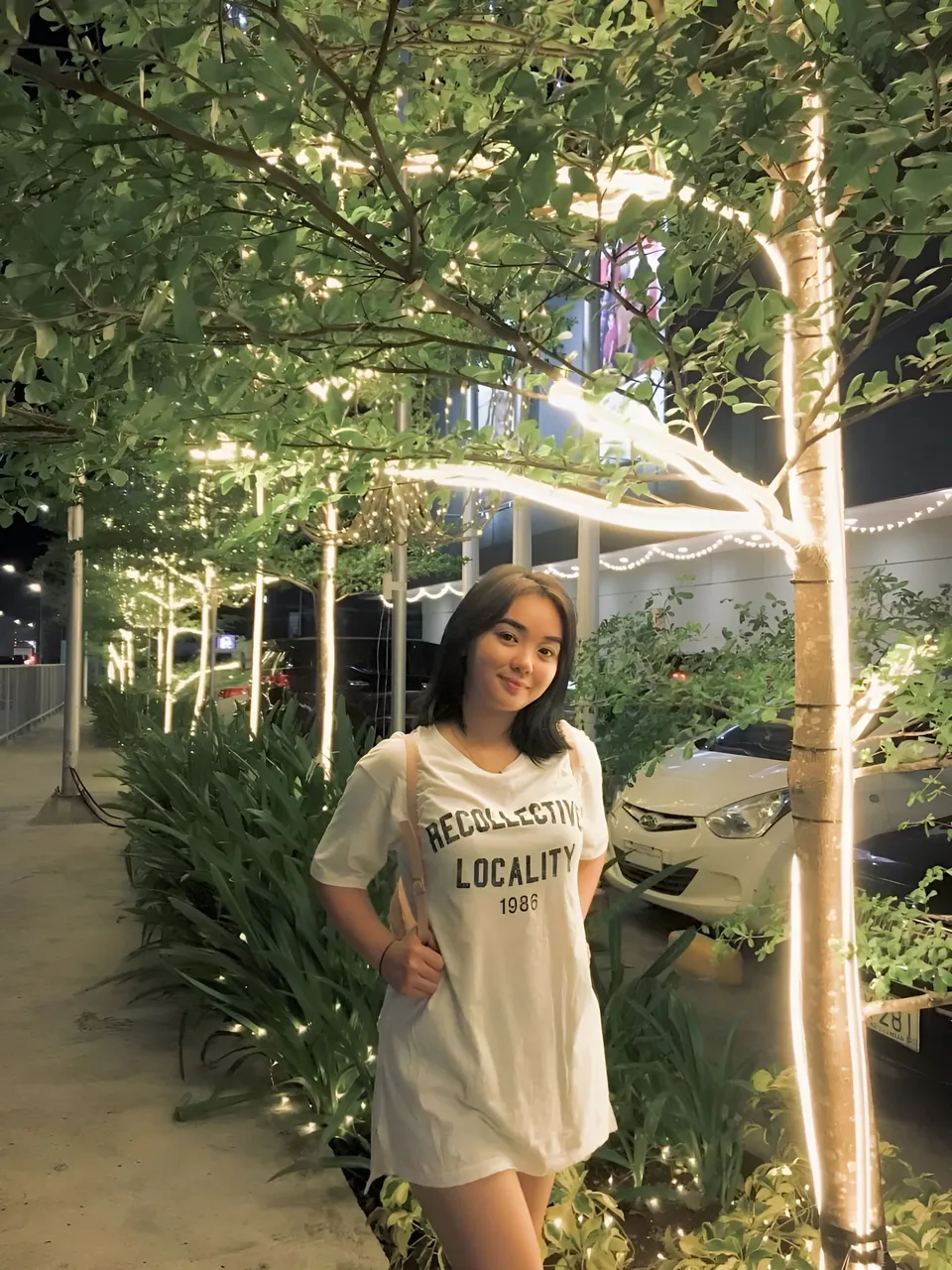 Sakura Keyema in white t-shirt stands under illuminated trees at night