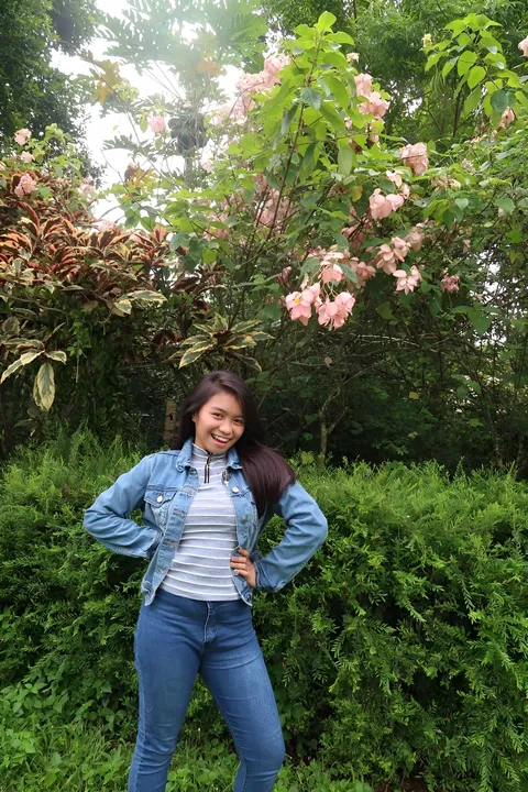 Samanta Shane Medalle in denim jacket and jeans standing outdoors near flowering bushes