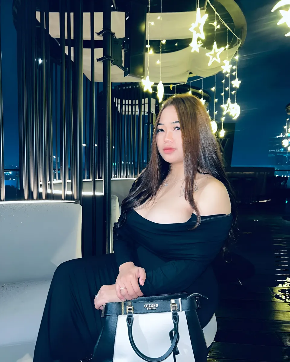 Serena Vale in black off-shoulder top seated with handbag