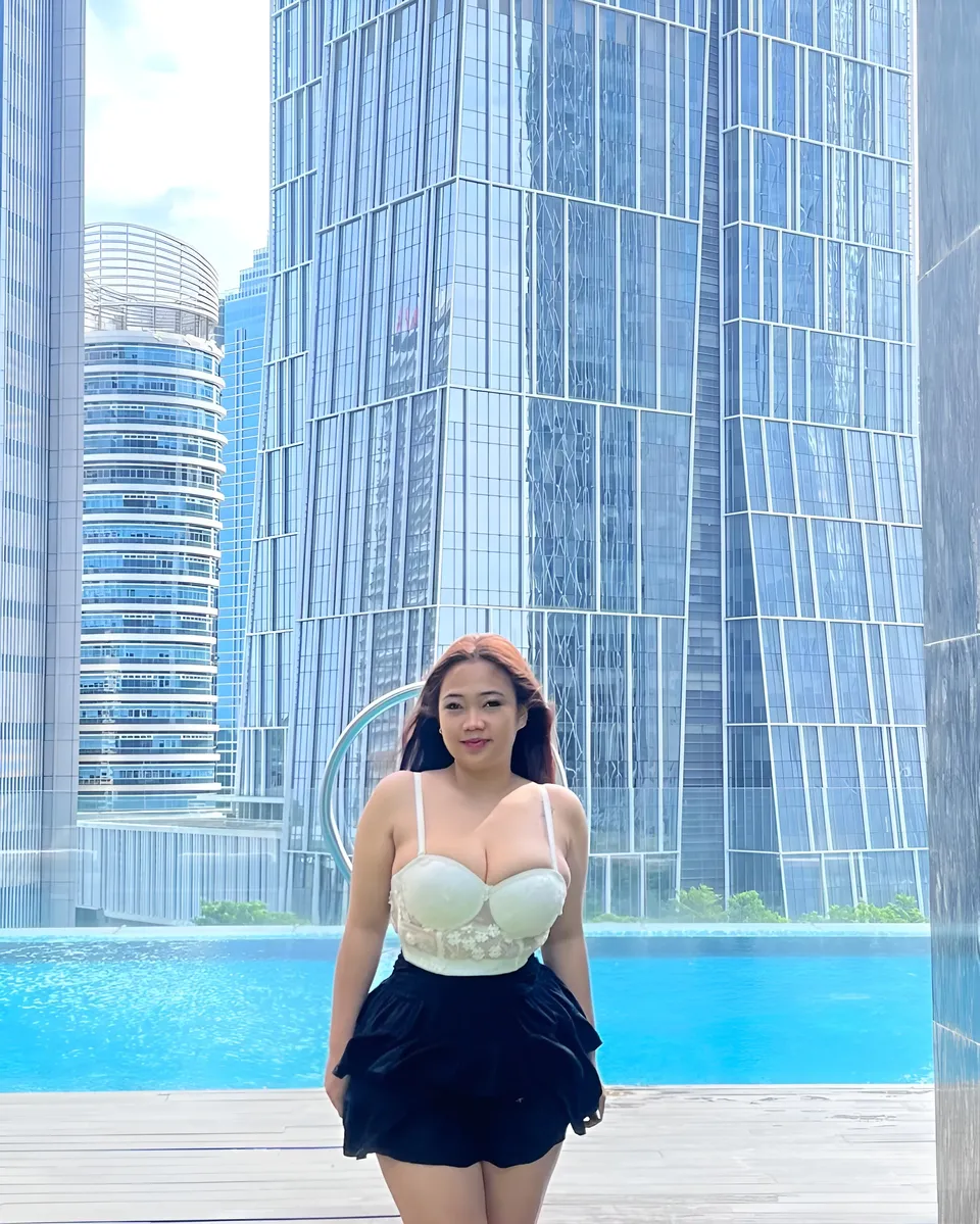 Serena Vale in white top and black skirt stands by swimming pool