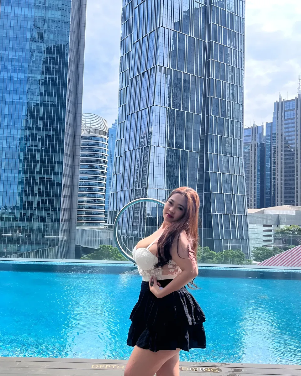 Serena Vale in white top and black skirt stands by rooftop pool