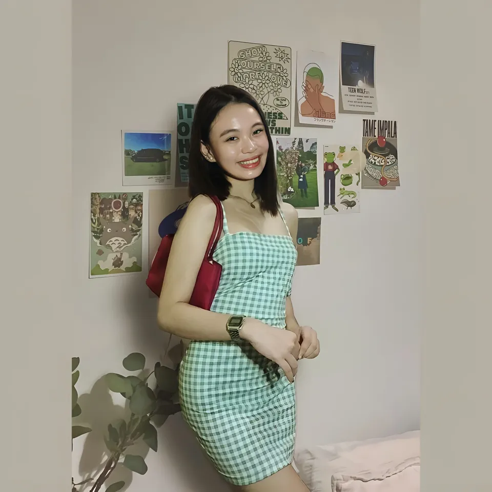 Shai Ponce in green checkered dress standing against wall with posters