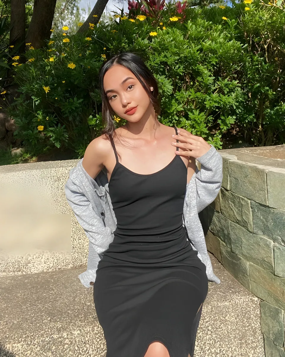 Shaira Adalyn in black dress and grey cardigan seated outdoors