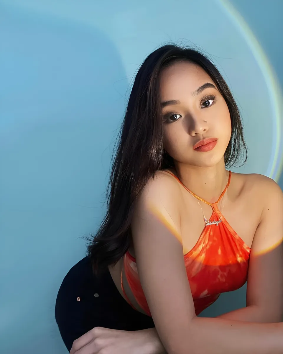 Shaira Adalyn in orange top seated against blue background