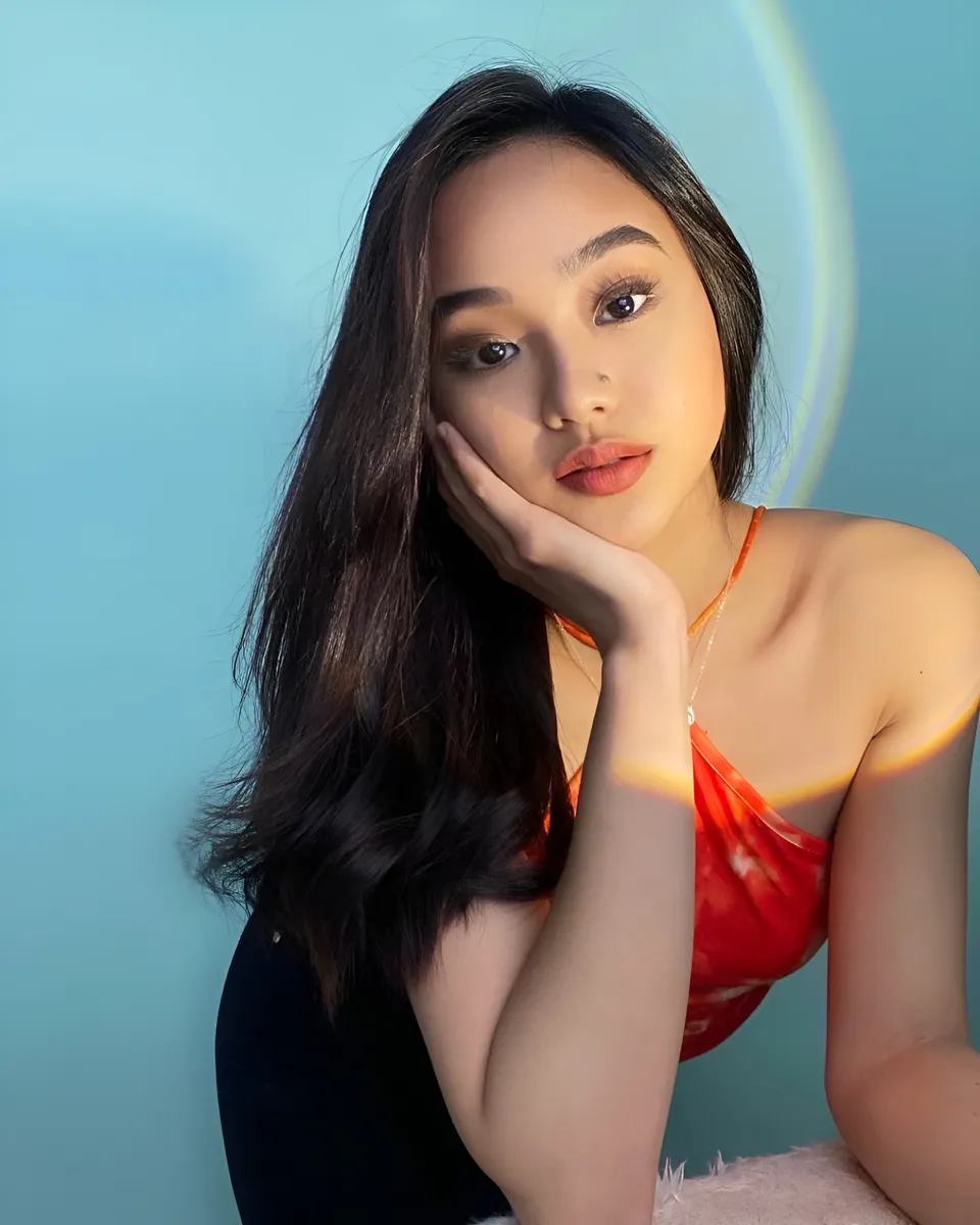 Shaira Adalyn in red top resting chin on hand against blue background