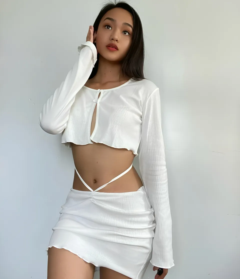 Shaira Adalyn wearing white cropped top and skirt, standing against plain wall