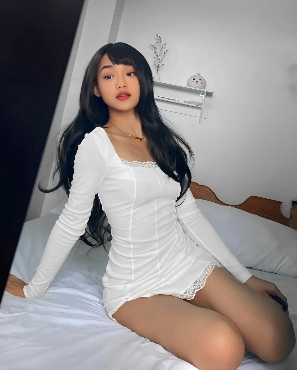 Shaira Adalyn in white dress sitting on bed
