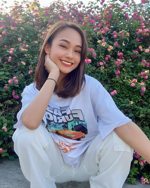 Shaira Adalyn in white t-shirt and pants crouching outdoors near flowers