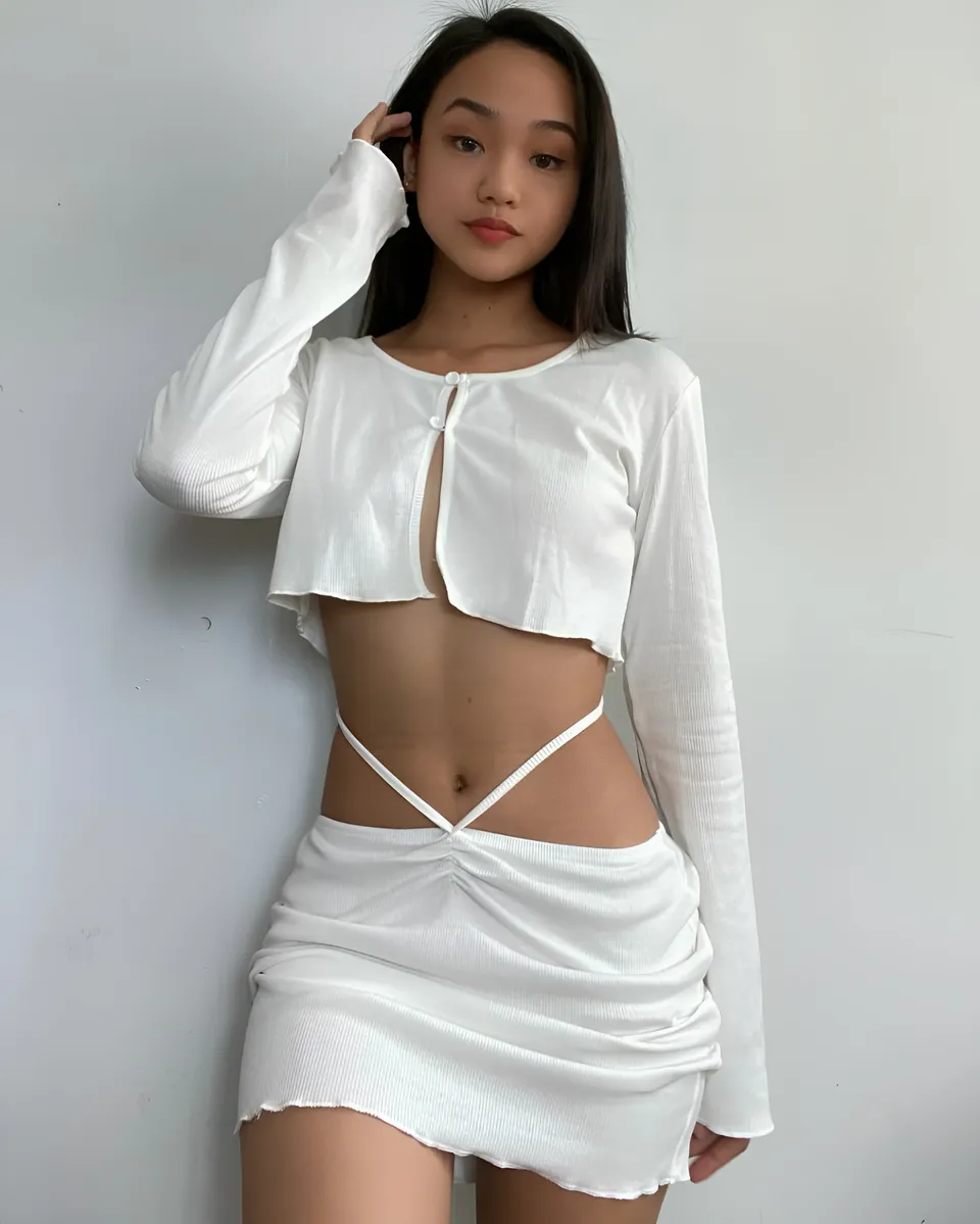 Shaira Adalyn wearing a white cropped top and skirt poses against a plain wall