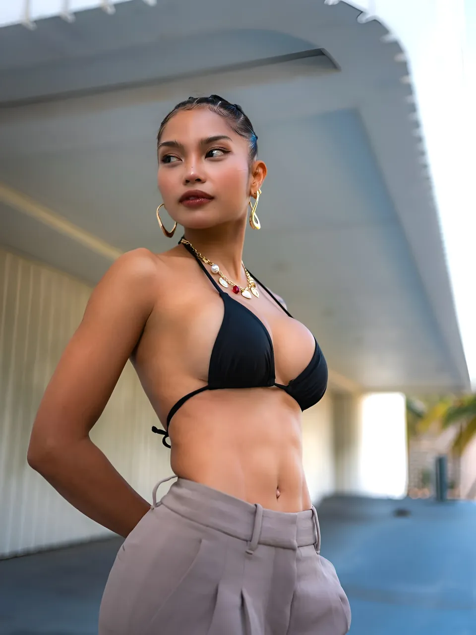 Sheeny Roswell in black bikini top and grey pants standing outdoors