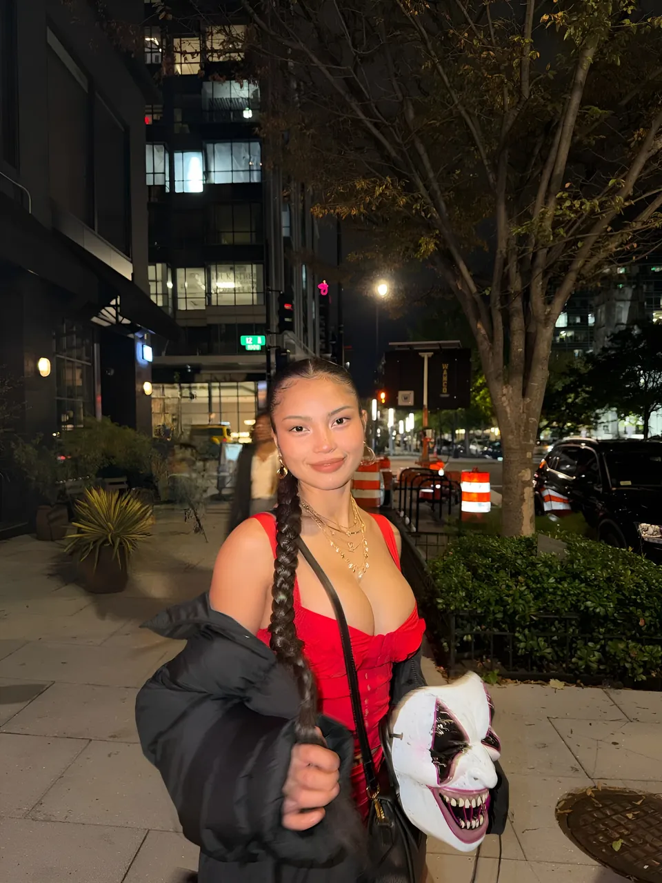 Sheeny Roswell in red top and black jacket holds mask outdoors at night