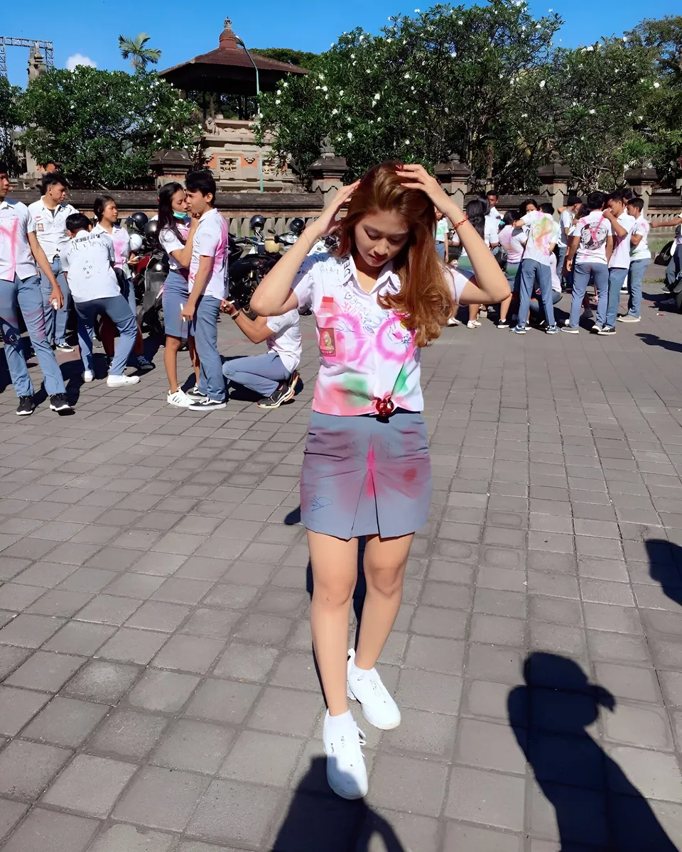 Sri Ayu Tarisa wearing a colorful shirt and gray skirt stands on a paved outdoor area