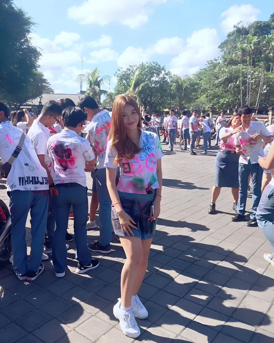 Sri Ayu Tarisa in colorful shirt stands among group outdoors on paved ground