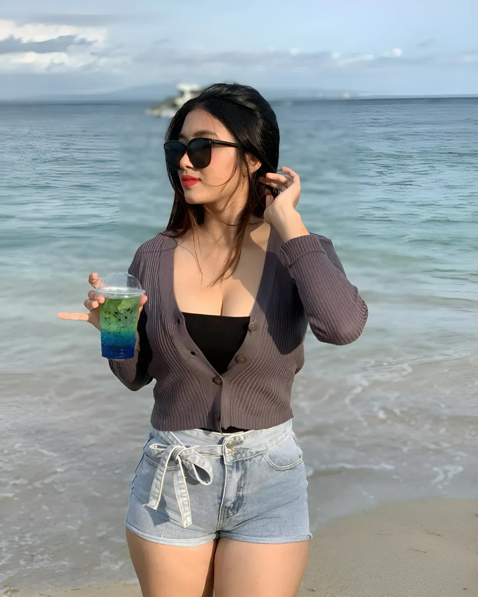 Sri Ayu Tarisa holding drink at beach with ocean in background