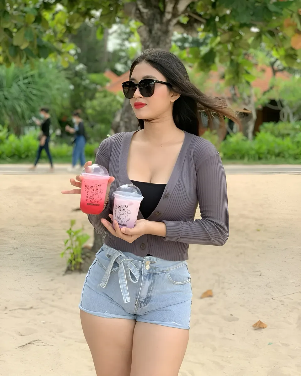 Sri Ayu Tarisa holding two drinks in park setting