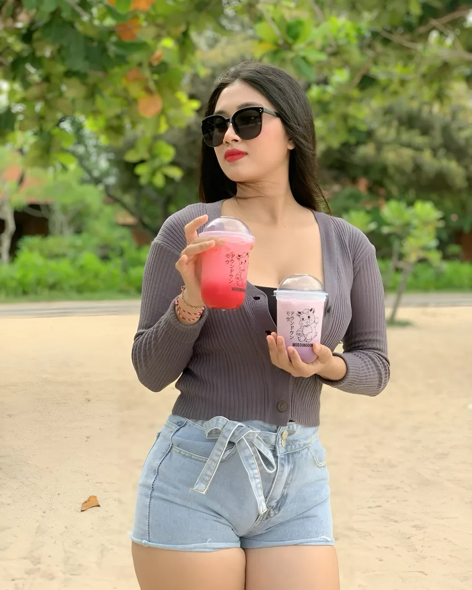 Sri Ayu Tarisa holding two pink drinks in outdoor setting