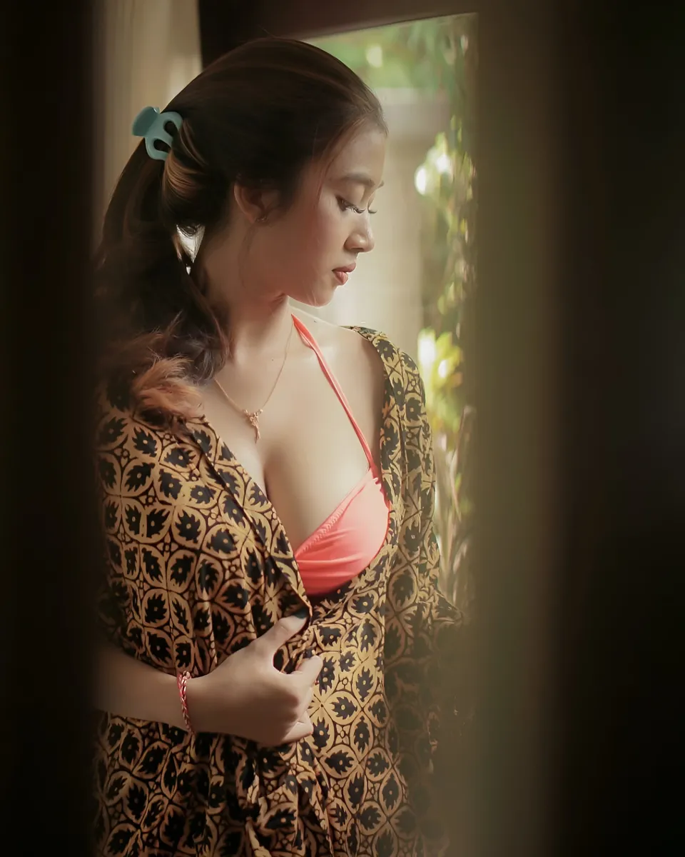 Sri Ayu Tarisa in patterned robe and bikini top standing by window