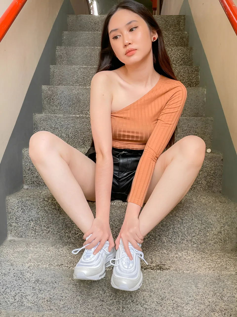 Stephanie Jean King sitting on stairs wearing orange top and white sneakers