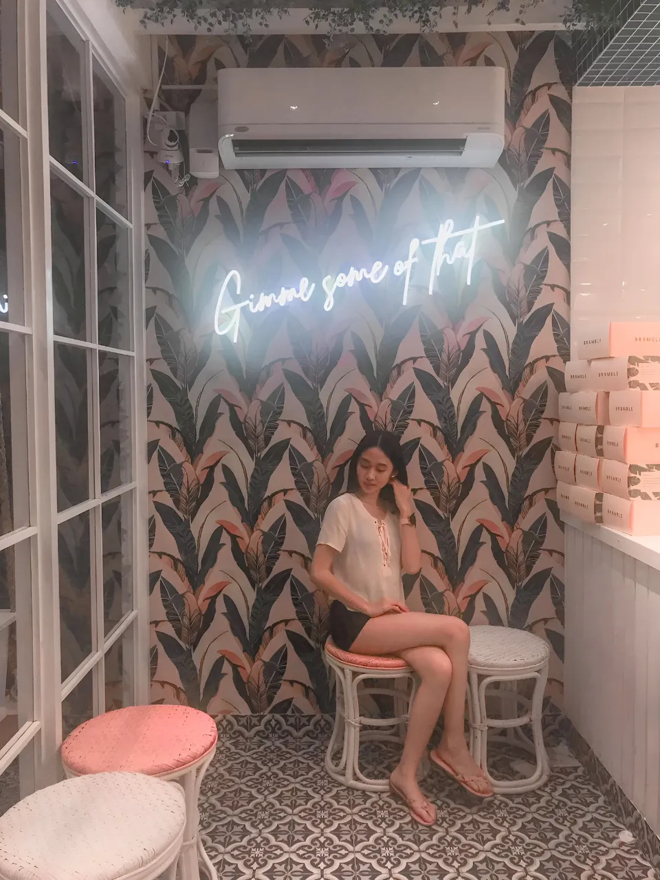 Stephanie Jean King sitting on stool in front of neon sign with leaf pattern wallpaper